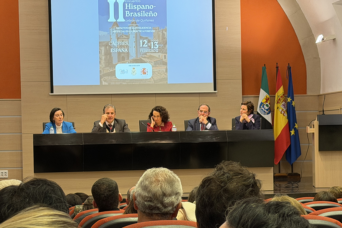  O Gemini disse A imagem mostra uma mesa redonda composta por cinco palestrantes sentados em um auditório, com as bandeiras da Extremadura, Espanha e União Europeia posicionadas à direita. Ao fundo, um telão exibe o cartaz do "II Encuentro Hispano-Brasileño", realizado em Cáceres nos dias 12 e 13 de fevereiro, abordando impactos da inteligência artificial. Em primeiro plano, a plateia é vista de costas, acompanhando o debate em um ambiente formal com paredes de madeira e detalhes em laranja
