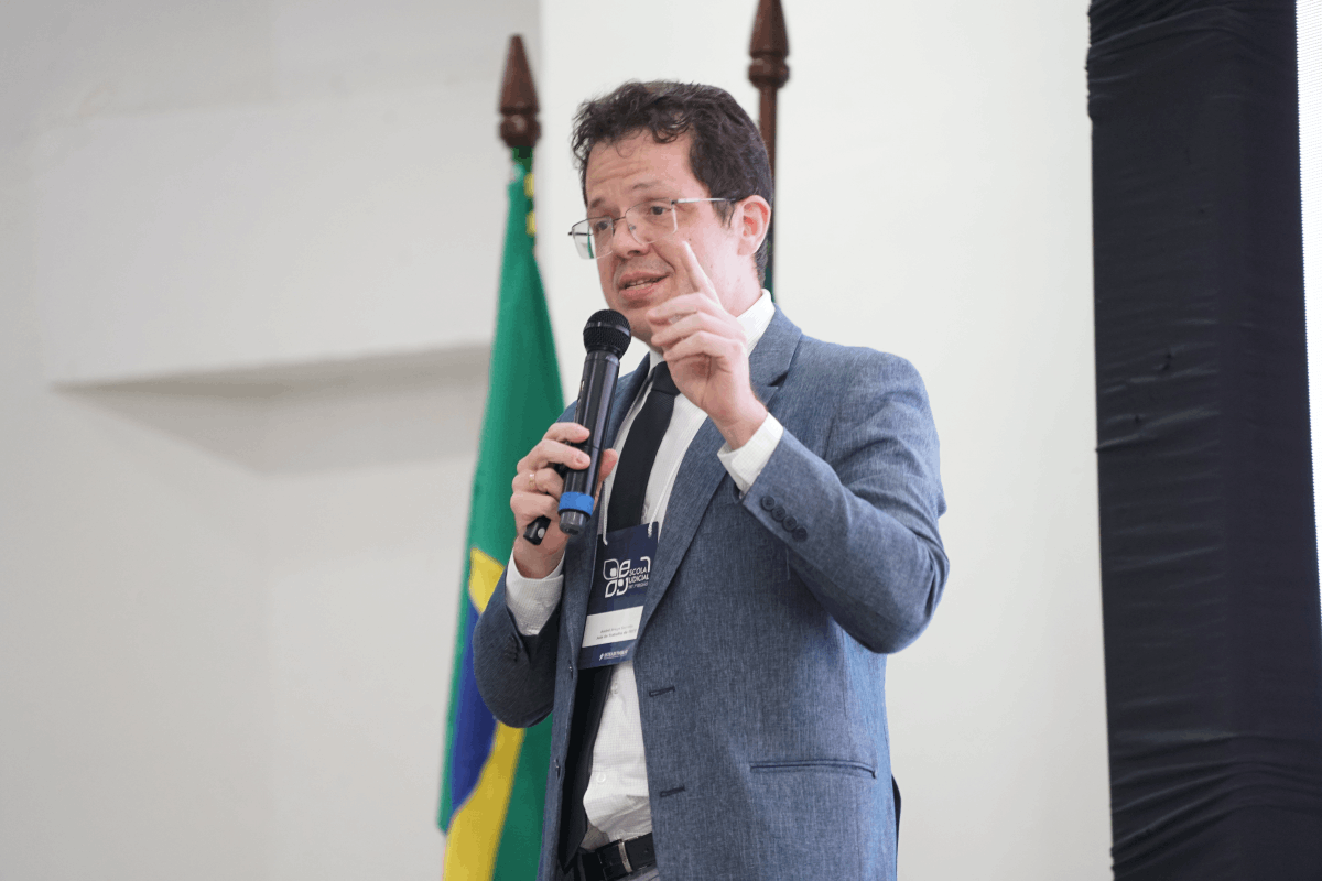 Card horizontal com fundo azul-marinho e grafismos geométricos em amarelo e azul claro. À esquerda, em uma moldura circular, a foto em preto e branco do Juiz André Barreto, que aparece sorrindo e usando terno e gravata. À direita, o texto destaca o nome do magistrado e o título da palestra: "Tema 1232 do STF e os Impactos na Execução Trabalhista", com logomarcas institucionais nas bordas.