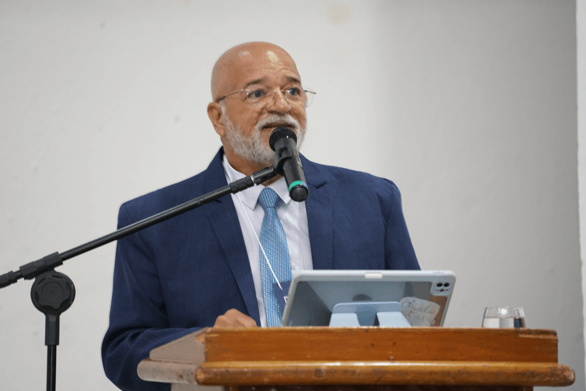 Card horizontal com fundo azul-marinho e grafismos em tons de amarelo e azul claro. À esquerda, em uma moldura circular, a foto em preto e branco do Desembargador Clóvis Valença Alves Filho, que aparece sorrindo e usando terno. À direita, o texto destaca o nome do magistrado e o título da palestra: "Contratação Formal via CLT ou PJ", com as logomarcas da Justiça do Trabalho no topo e rodapé.
