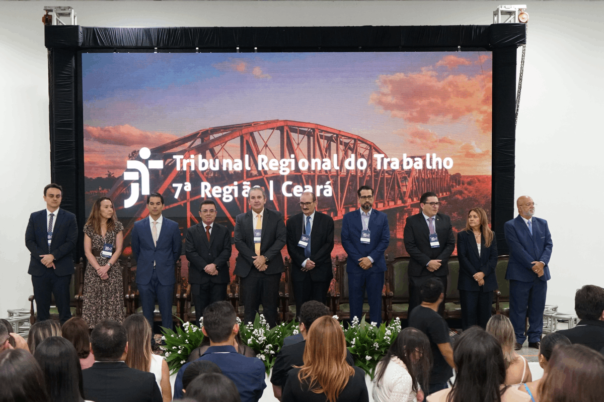 Card horizontal com fundo azul escuro e detalhes geométricos em amarelo. No topo, logomarcas da Justiça do Trabalho, TST, CSJT e TRT da 7ª Região (Ceará). O título central em branco e amarelo diz: "Seminário: Os Desafios do Novo Mundo do Trabalho e a Efetividade da Execução Trabalhista no Cariri e Centro-Sul". Na parte inferior, as informações: "10 de abril | 9h às 17h", local "Iguatu - Ceará" no Sesc Iguatu, e inscrições via Sympla com QR Code flanqueando o texto.