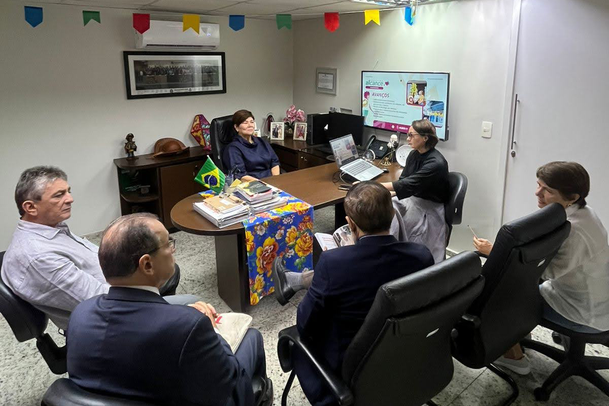 um grupo de seis pessoas realiza uma reunião de trabalho em um escritório decorado com bandeirinhas juninas, concentrado em torno de uma mesa com documentos e notebooks.
